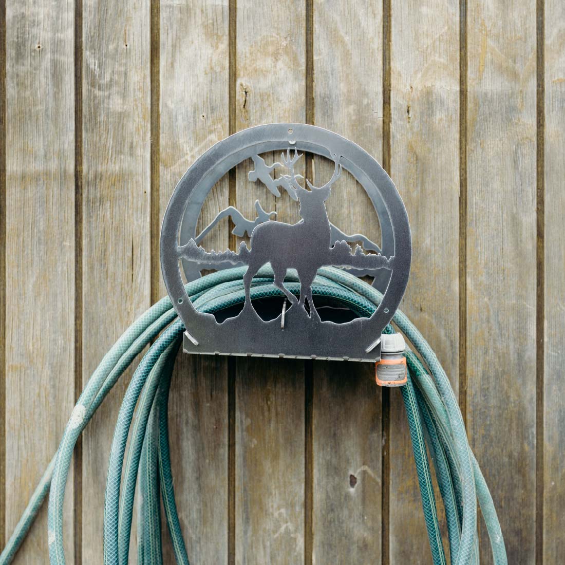 Metal hose holder with deer design attached to a coiled green garden hose against a wooden fence.
