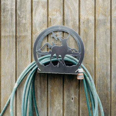 Metal hose holder with deer design attached to a coiled green garden hose against a wooden fence.
