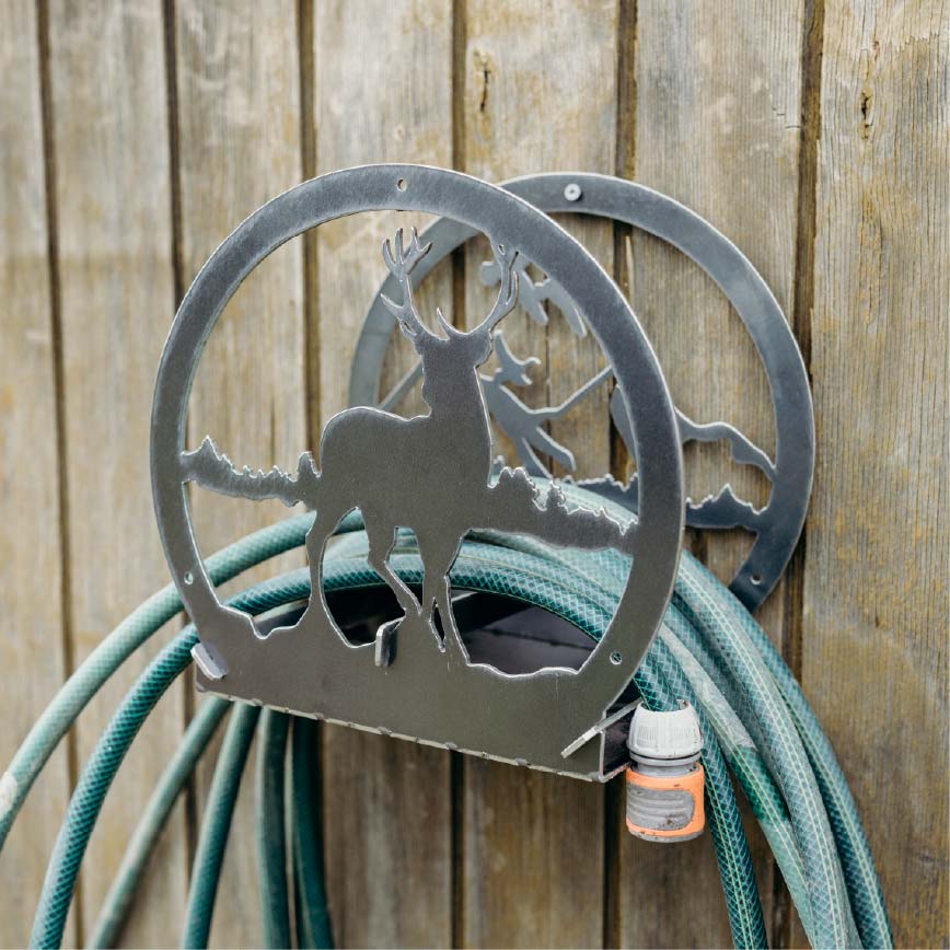 Metal hose holder with deer design attached to a wooden fence with a green garden hose.