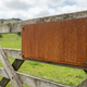 A weathered rusted Corten steel sign on a rural New Zealand farm gate