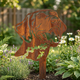 A rusted Corten steel dog silhouette memorial in a peaceful garden