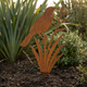 Rusted Corten steel tui on flax garden sculpture staked in a New Zealand garden bed