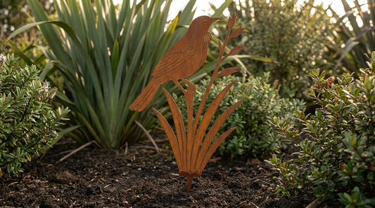 Rusted Corten steel tui on flax garden sculpture staked in a New Zealand garden bed