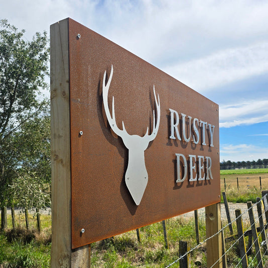 Metal sign with antler design and 'Rusty Deer' text on a wooden post against a blue sky.