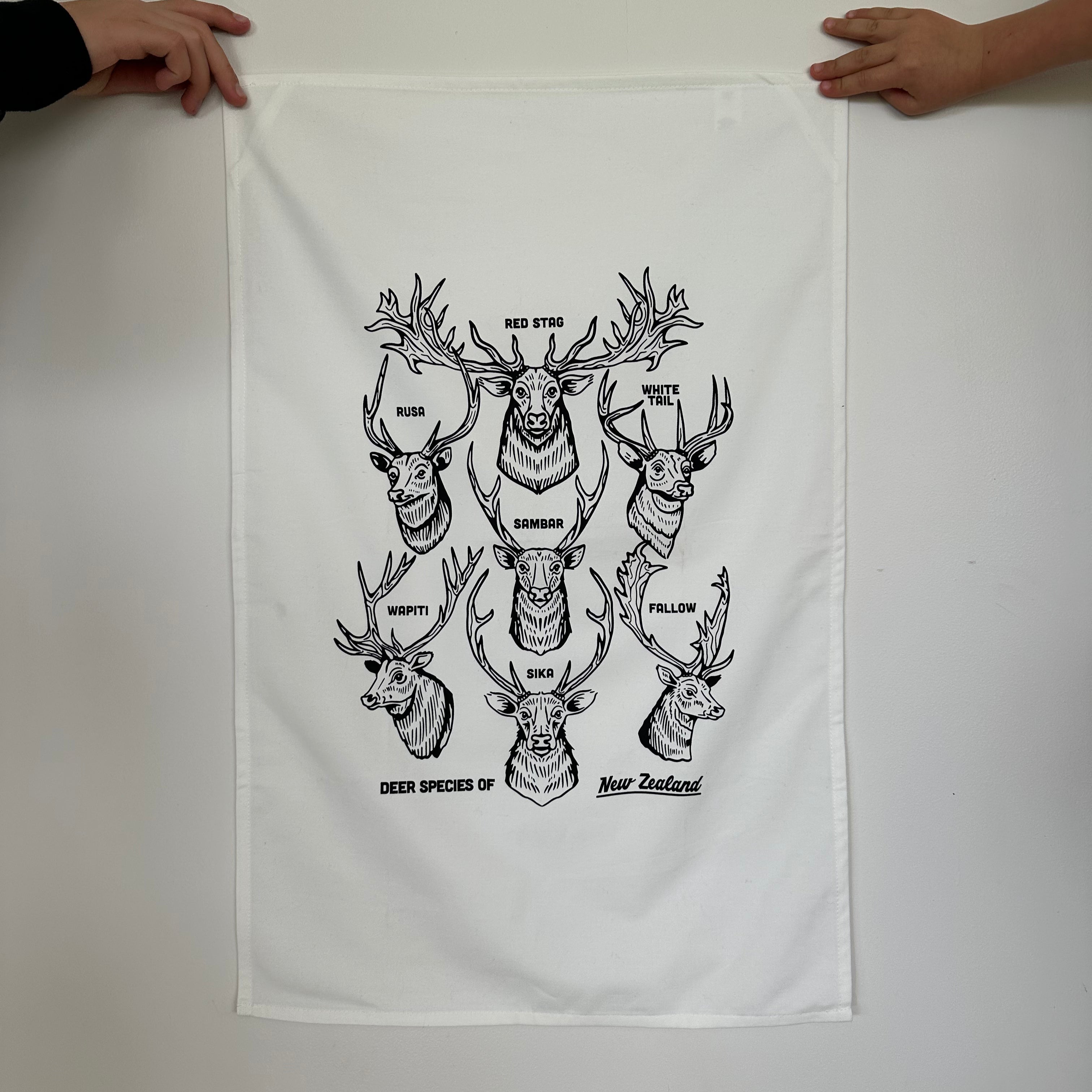 White towel with black deer head illustrations held by two people on a white background