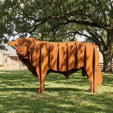 Cow wearing a brown coat in a grassy field with trees and a building in the background