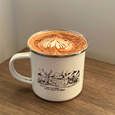 White mug with nature-themed design filled with a hot beverage on a wooden surface.