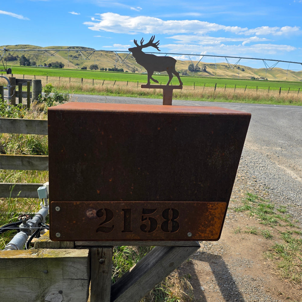 Metal sign with Deer design and number 2158 on a rural road with grass and sky.