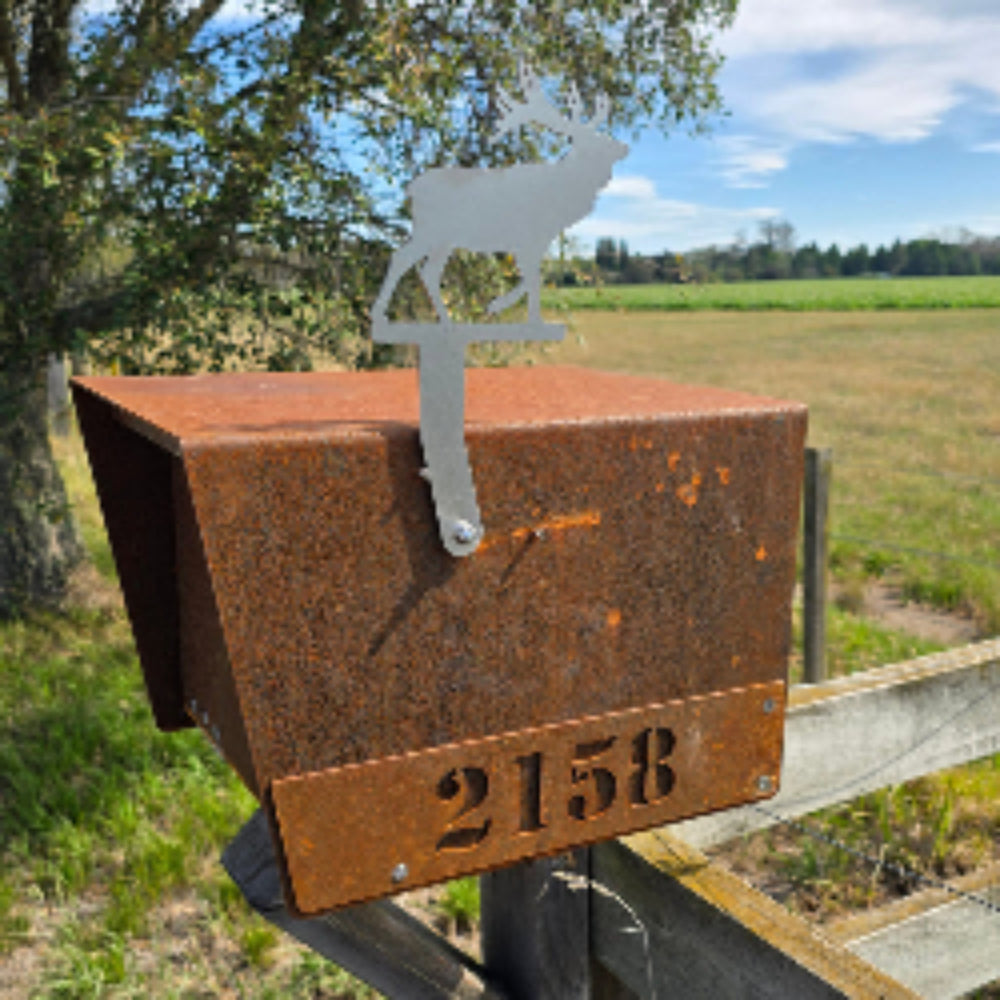 Rust-colored metal box with a number on a wooden post, surrounded by trees and sky.
