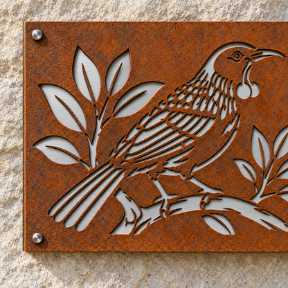Close-up of the Tui House Number Corten front, precise tūī and leaf cutouts, and brushed stainless steel backing.