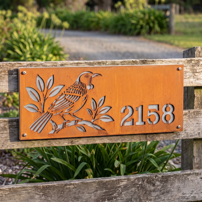 Tui House Number in weathered Corten steel with brushed stainless steel backing, installed on a timber fence; example number 2158.